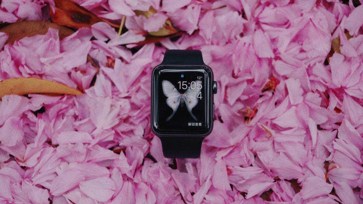 Smartwatch with pink butterfly on screen in black color smartphone, and pink floral petals in the background.