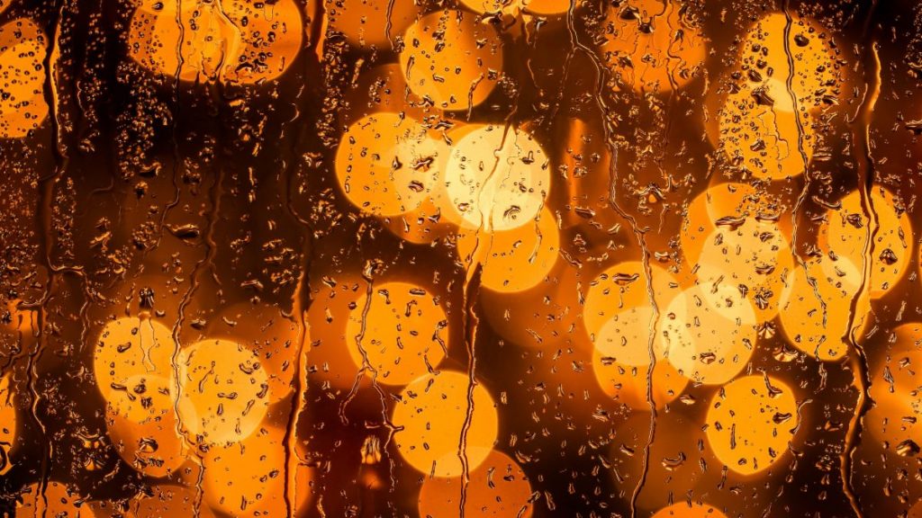 Orange circular lights blurred at a distance with rain water hitting against a glass.