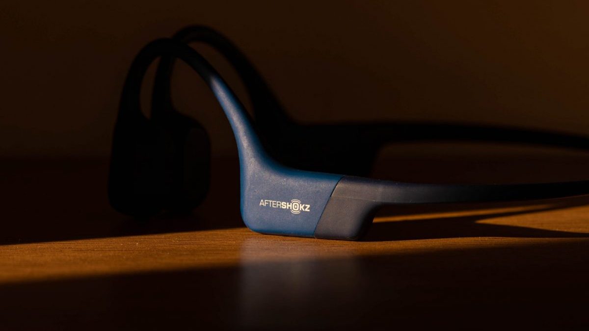 A Shokz bone conduction headset resting on a table in a dark room with a little light beaming in.