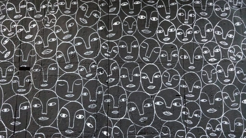 many facial expressions drawn on a dark color in white marker.